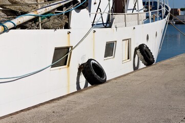 Old white fishing boat with fishing equipment and tires as fender (Pesaro, Italy, Europe)
