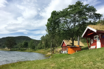 Obraz premium red wooden houses with a grass roof in the Scandinavian style on the lake