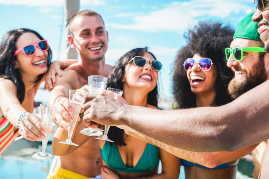 Happy friends cheering with champagne in summer boat party - Young people having fun drinking and laughing together - Youth lifestyle and vacation concept - Focus on right black hand