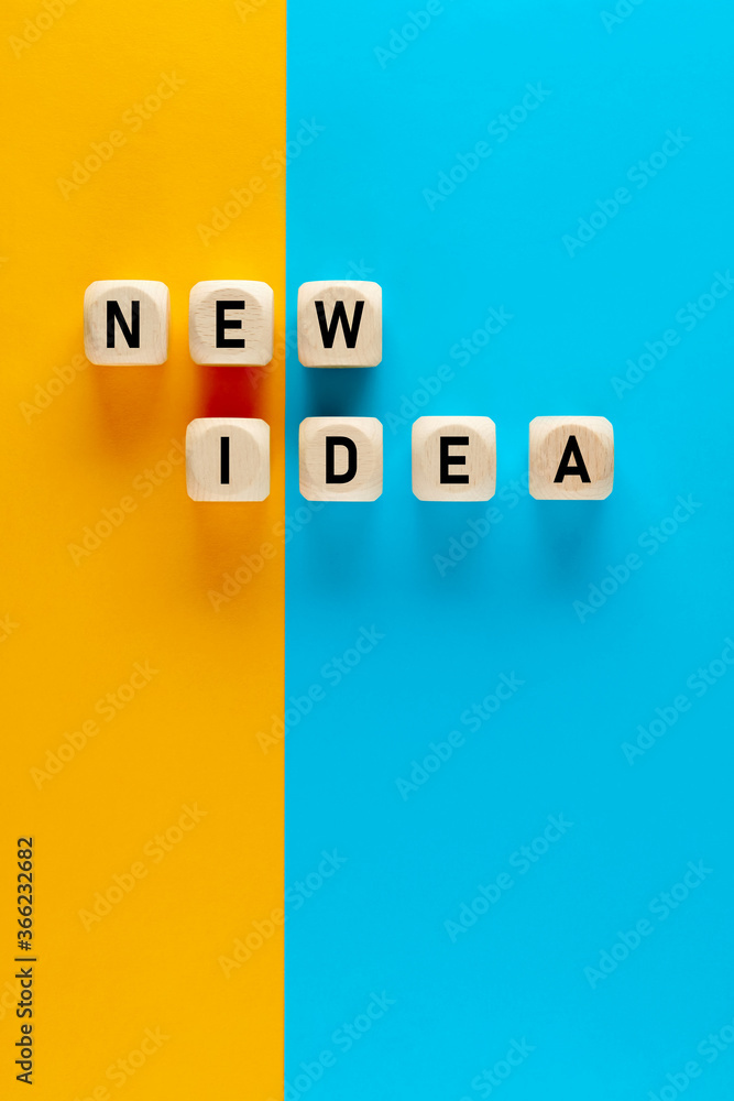 Poster the word new idea written on wooden cubes on yellow and blue background. finding and implementing ne