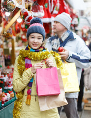 Fototapeta na wymiar Preteen girl looking happy with bags while shopping on Christmas street fair with her father