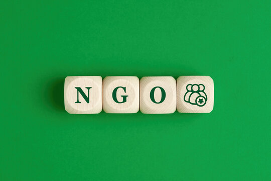 The Abbreviation Word NGO Nongovernmental Organization Written On Wooden Cubes With Group Of People Icon On Green Background