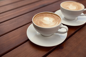 Two cups of cappuccino on the wooden background. Beautiful brown foam, white ceramic cups, place for text