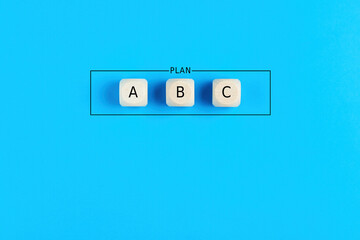 Plan a, b and c on wooden cubes on blue background. Choosing a business strategy plan out of three...