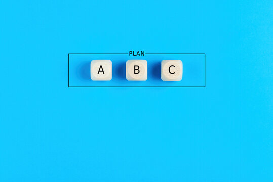 Plan a, b and c on wooden cubes on blue background. Choosing a business strategy plan out of three options.