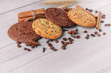 Freshly baked oat and chocolate cookies on a white wooden table background with coffee beans, anise, cinnamon sticks, cloves, wheat with copy space. Image design for menu layout. front view