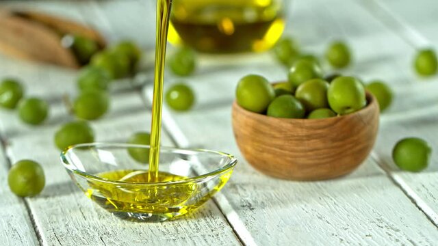 Super Slow Motion Shot of Pouring Fresh Olive Oil into Glass Bowl on White Wooden Table at 1000 fps.