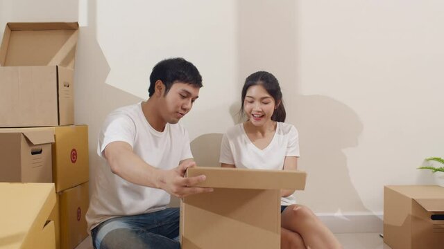 Happy Asian young couple bought new house. Korean family opening unpacking cardboard boxes and easy and fast service commerce delivery into big modern home. New real estate dwelling, loan and mortgage