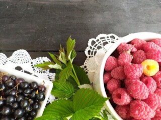 Fruit still life white ceramic bowl with ripe red raspberries and black currant on lace napkin on black wooden table