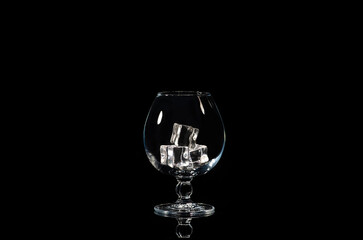 an empty cognac glass with ice cubes on a black background with reflection.