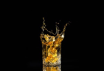A glass of whiskey with splashes from the ice cube over black background. alcohol splashes. whisky or cognac or another type of alcohol with splashes.