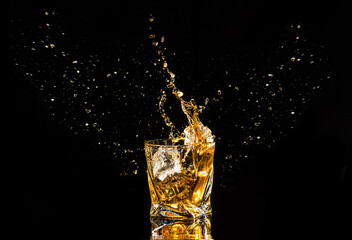 A glass of whiskey with splashes from the ice cube over black background. alcohol splashes. whisky or cognac or another type of alcohol with splashes.