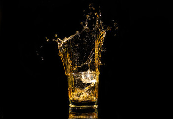 A glass of whiskey with splashes from the ice cube over black background. alcohol splashes. whisky or cognac or another type of alcohol with splashes.