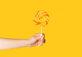 Young woman holding swirl lollipop over orange background, close up of hand