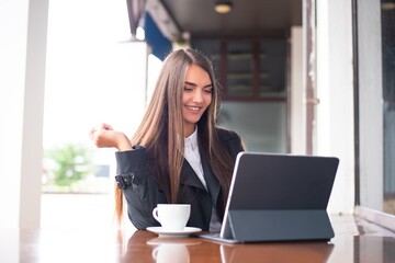 Cute young business women is sitting outdoor with a tablet, speaking with somebody and laughing.