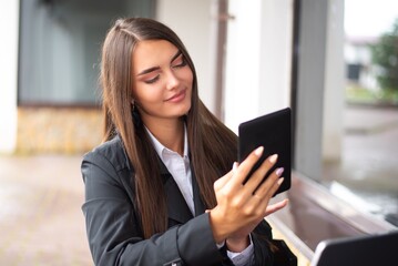 Beautiful young women in a black coat is sitting at a restaurant and watching to a tablet and smiling.