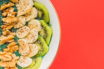 spirulina smoothie bowl with banana, walnuts, kiwi and chia seeds on red background