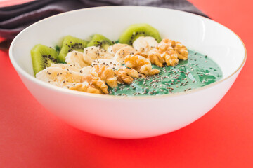 spirulina smoothie bowl with banana, walnuts, kiwi and chia seeds on red background
