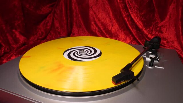 Stylus arm and needle lowered on 12&rdquo; yellow splatter vinyl record on DJ turntable red velvet background. Retro LP platter. Mid Shot. Disco, hip-hop, reggae, punk, grunge, pop 60s, 70s, 80s, 90s 4K