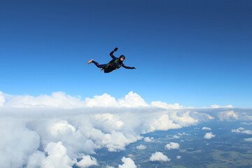 Skydiving. A skydiver is flying above white clouds.