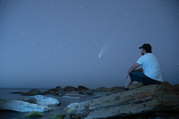 man sitting down looking at neowise comet at night