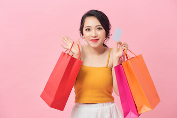 Portrait of a beautiful girl wearing dress and holding colorful shopping bags and showing credit card isolated over pink background