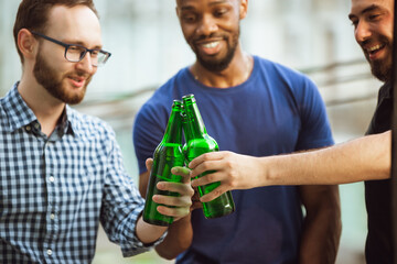 Group of happy friends having beer party in summer day. Resting together outdoor, celebrating and relaxing, laughting. Summer lifestyle, friendship concept. Clinking beer's bottles, look cheerful