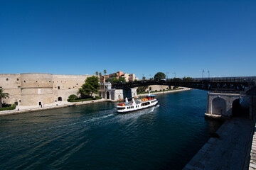 Fototapeta na wymiar small boat that cross the swing bridge in front of the aragonian castle in taranto on blue sky background