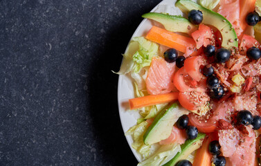 Summer salad with smoked salmon, carrots, tomatoes, avocado, ginger, blueberries, goji berries, fresh vegetables, ice salad, linseed seeds