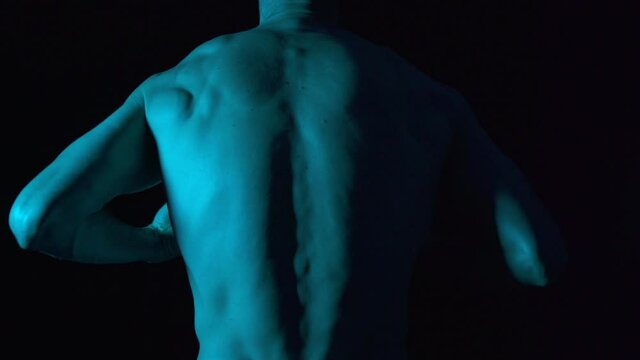 Back naked body torso male warming up for martial arts. Dancer movements in black background and red lighting.