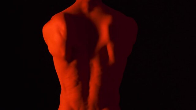 Back naked body torso male warming up for martial arts. Dancer movements in black background and red lighting.