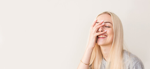 Vivacious woman giglling with her eyes screwed up in a moment of fun as she sitting against beige studio wall. Happy natural laughing young casual female covering mouth. Human face expressions