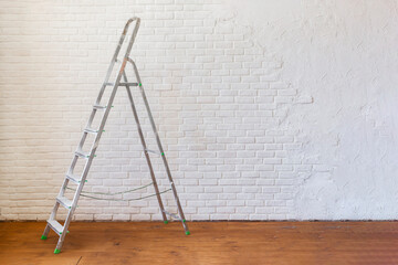 A construction ladder stands on a wooden floor. - obrazy, fototapety, plakaty