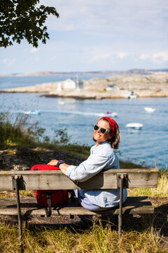A young woman sitting on a bench and enjoying a view over the Swedish west coast, Sweden