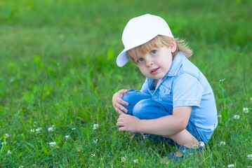 A child in a white cap sits in the Park on the grass.