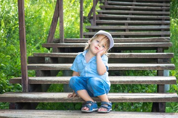A sad boy is sitting on a wooden staircase in the Park and is bored.