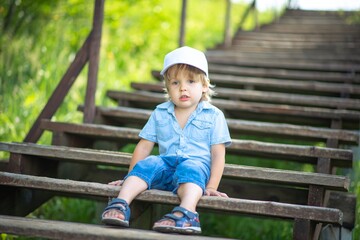 A sad boy is sitting on a wooden staircase in the Park and is bored.