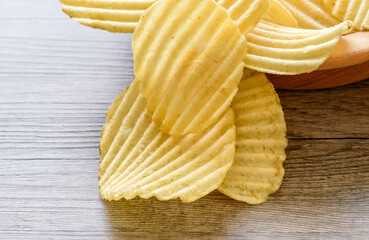 Corrugated golden potato chips in a wooden bowl on rustic wooden table.