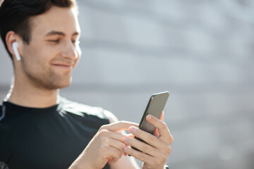 Favorite track for training and great mood. Smiling guy in sportswear with wireless headphones looks at smartphone