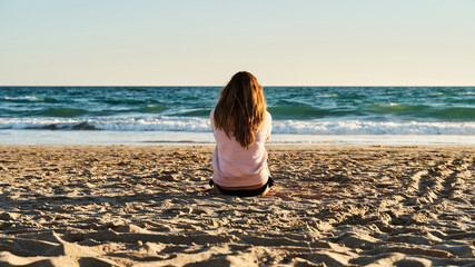 Young woman sitting on the sand on the beach, watching the sunset. Concept of beach, vacation and travel. - 366252068