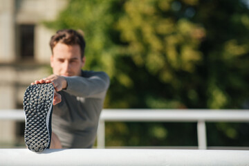Flexibility and exercise. Muscular guy puts his foot on railing and does stretching or exercise