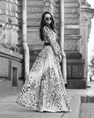 Young beautiful pretty caucasian young woman with brunette wavy hair wearing long gray summer dress and walking at city street on a summer day