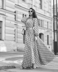 Pretty stylish woman wearing yellow and white polka-dot sundress and sunglasses. Beautiful girl in long dress walking and standing at city street