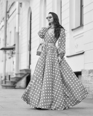 Pretty stylish woman wearing yellow and white polka-dot sundress and sunglasses. Beautiful girl in long dress walking and standing at city street