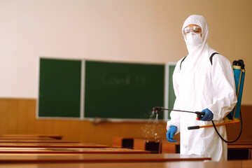 Disinfecting schools during coronavirus pandemic. Man wearing protective suit disinfecting school...