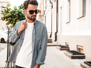 Portrait of handsome confident stylish hipster lambersexual model.Man dressed in white T-shirt. Fashion male posing on the street background in sunglasses