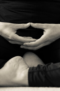 Vertical BW detail of hands and feet of young woman meditating indoors. Yoguini making contemplative hand gesture Dhyana Mudra during meditation exercise, hands placed on lap and palms facing upward