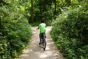 one nine-year-old boy riding a bicycle down a dirt road in a lush green park