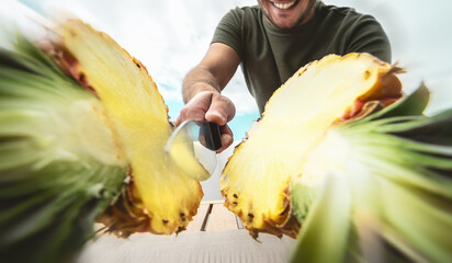 Young smiling man cutting pineapple - Close up male hand holding sharp knife preparing tropical fresh fruits - People lifestyle and healthy exotic food concept © Alessandro Biascioli