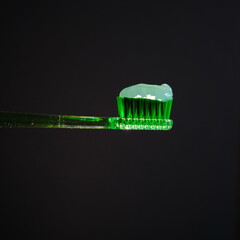 Green transparent toothpaste on Green toothbrush on black background